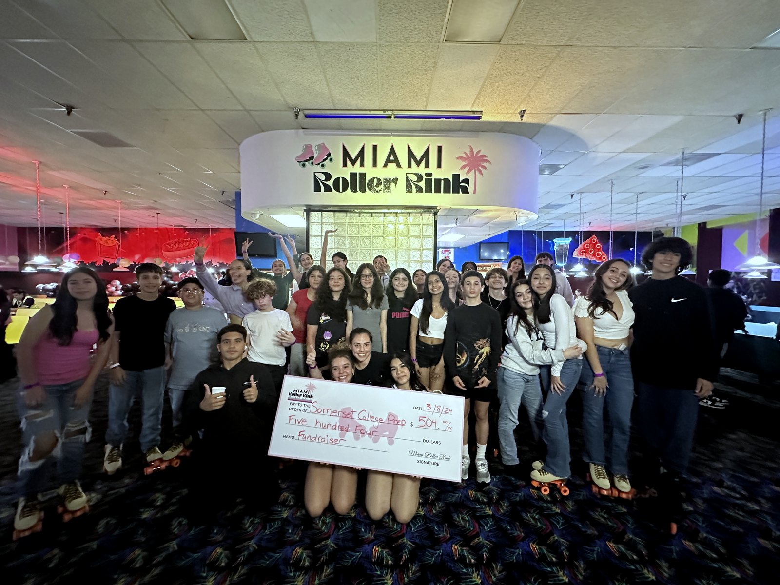 A community group holding a large fundraiser check at the Miami Roller Rink entrance