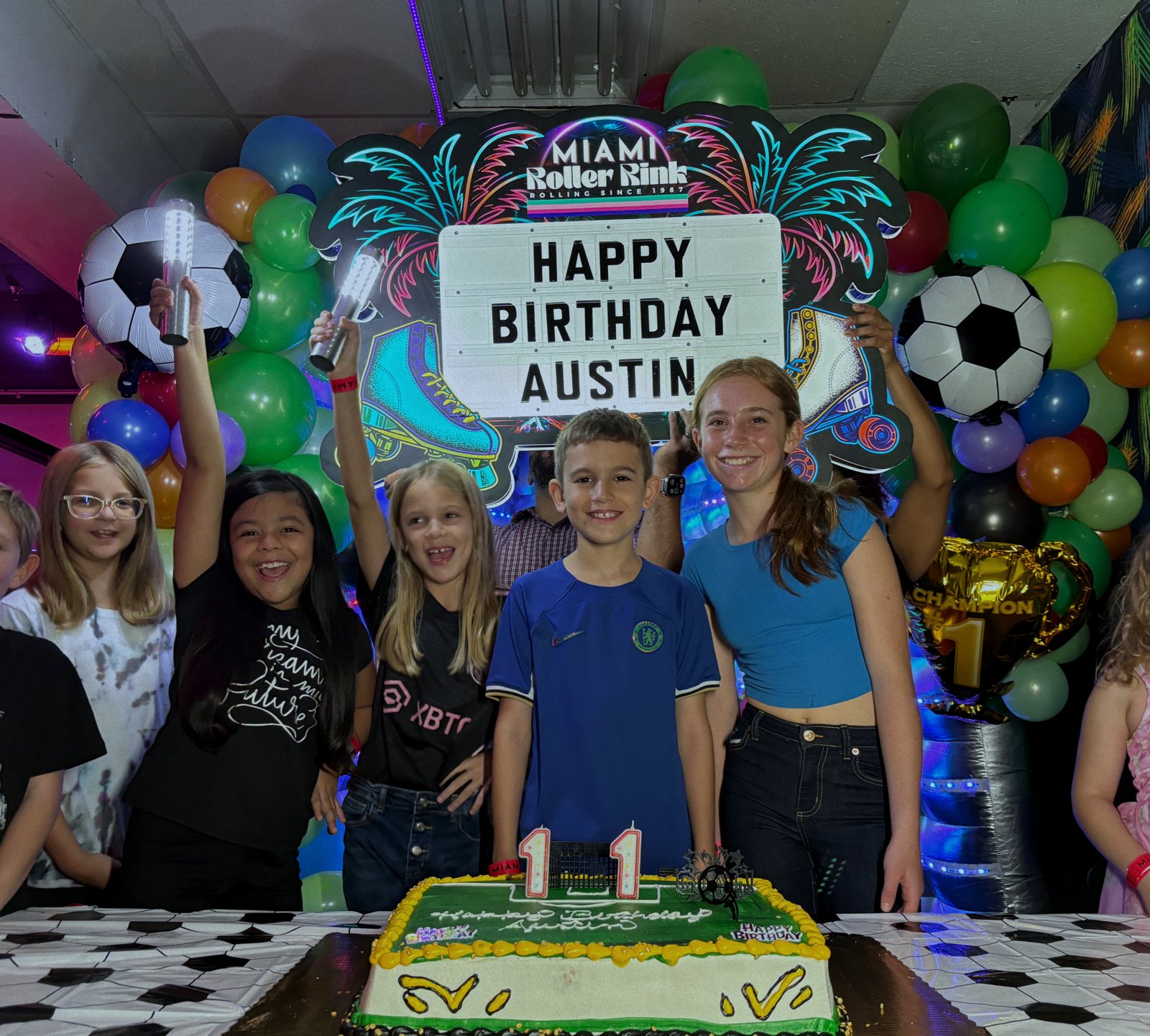 Kids gathered around a birthday cake with balloons at a Miami Roller Rink party